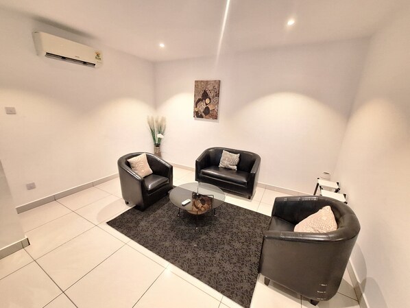A modern living room with two black leather sofas, a glass coffee table, and a dark patterned rug.