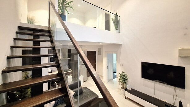 A modern interior with a staircase leading to a loft area, a flat-screen TV, and potted plants. - The Gem of Embassy Gardens  (Accra)