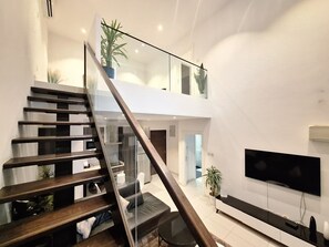 A modern interior with a staircase leading to a loft area, a flat-screen TV, and potted plants.