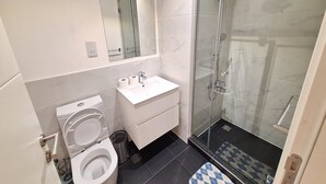 A modern bathroom with a toilet, sink, mirror, and glass-enclosed shower. - The Gem of Embassy Gardens  (Accra)