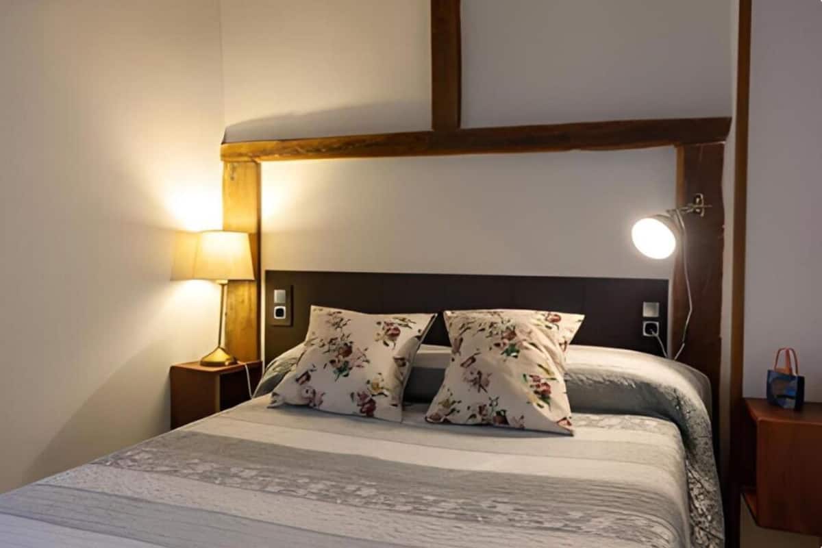 A neatly made bed with floral pillows, a bedside lamp, and a wall-mounted light fixture.