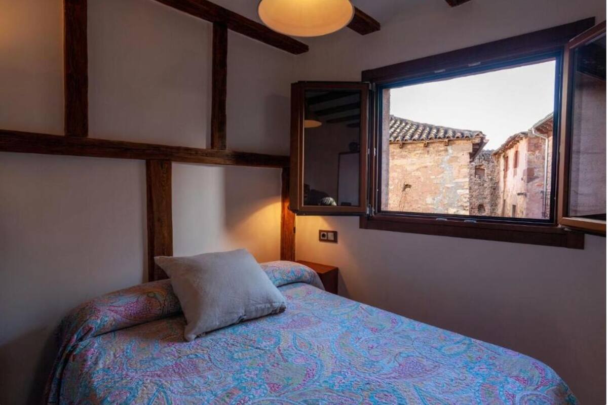 A bedroom with a bed, a window with a view of buildings, and wooden beams on the ceiling.
