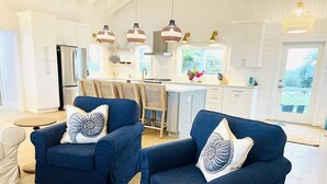 A modern kitchen with white cabinetry, a dining area with a round table, and two blue armchairs with decorative pillows.