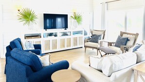 A living room with a large flat-screen TV, a blue sofa, a beige sofa, and a wooden coffee table.