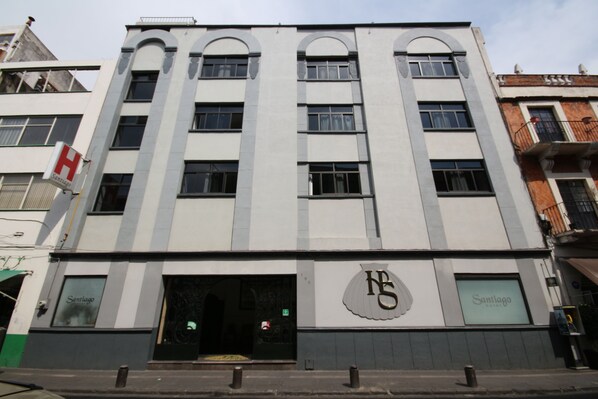 Un edificio de varios pisos con un llamativo letrero en forma de 'H' a la izquierda, un gran logo 'HS' en la fachada y un letrero que dice 'Santiago' en la planta baja.