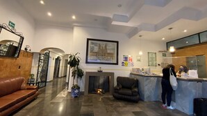 A hotel lobby with a reception desk, a brown leather sofa, a fireplace, and a large framed picture on the wall. - HOTEL SANTIAGO (Puebla)