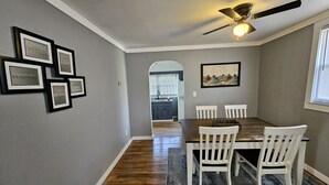 Un coin repas avec une table en bois et des chaises blanches, des citations inspirantes encadrées au mur et un ventilateur de plafond.