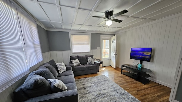 Un salon avec un canapé d’angle, un téléviseur et un ventilateur de plafond.