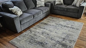Un salon avec un canapé d’angle gris, un tapis gris et un plancher en bois.