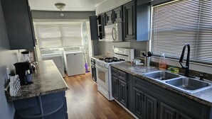 Une cuisine moderne avec des meubles de couleur gris foncé, un plan de travail en granit, des appareils électroménagers en acier inoxydable et une fenêtre équipée de stores.