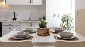 A modern kitchen with white cabinets, a dishwasher, and a sink. There is a dining table set with white plates, bowls, and wine glasses. A wooden crate with plants is placed on the table. - Malvarrosa Las Arenas Access. WiFi + Air Conditioning + 5 Pax (Valencia)