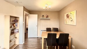 Un comedor con una mesa de madera y cuatro sillas, una estantería, una puerta blanca y un estante montado en la pared con objetos decorativos.