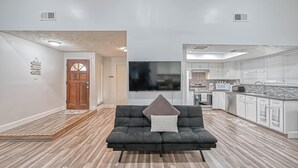 A modern living room with a black sofa, a flat-screen TV, and a kitchen area with white cabinets and a countertop. - Spacious 3-bedroom house in beautiful Houston with AC (Houston)