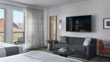 Habitación de hotel con cama, sofá, mesa de centro, televisión y vistas a las montañas.