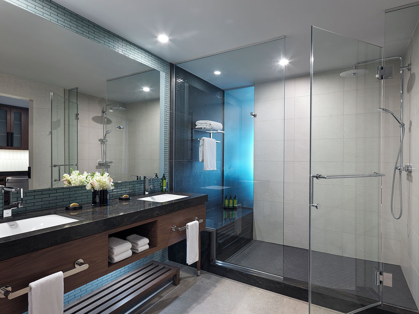 Une salle de bain moderne avec une douche à parois de verre, un meuble-lavabo en bois foncé et un grand miroir.