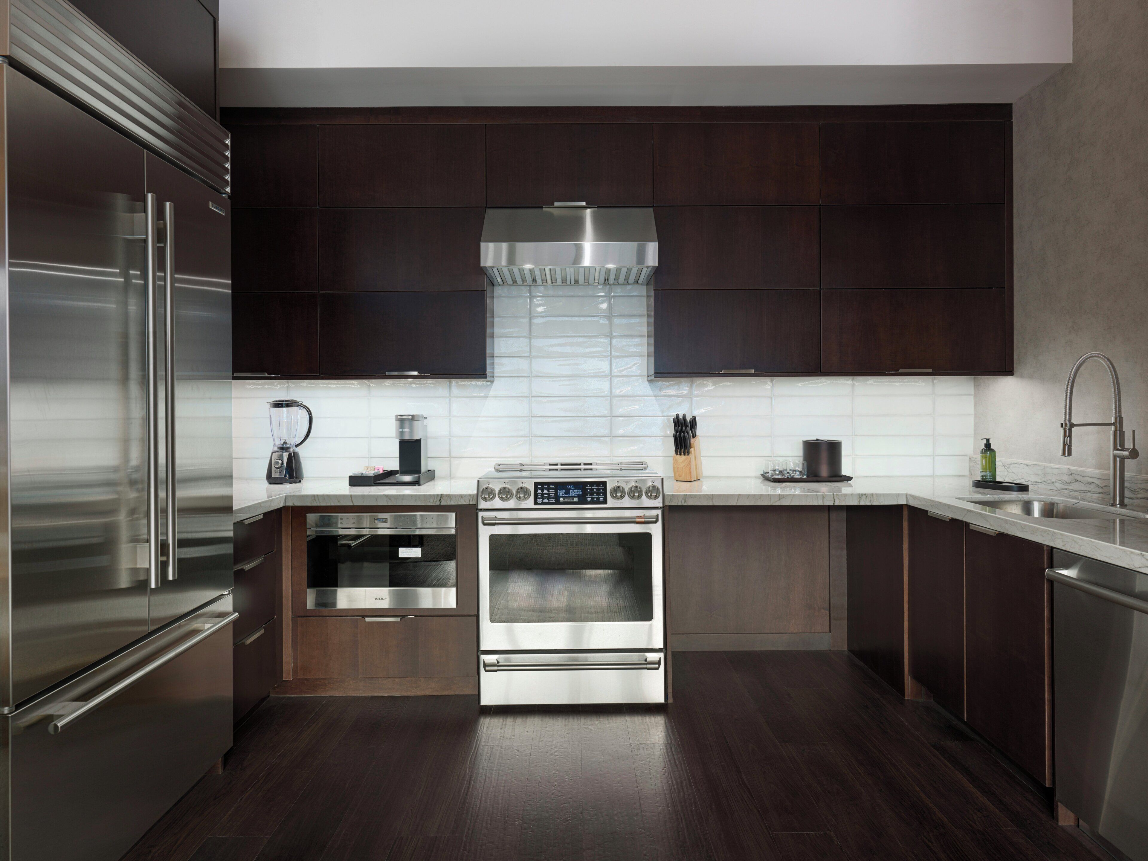A modern kitchen with dark wood cabinets, stainless steel appliances, and a white tiled backsplash.