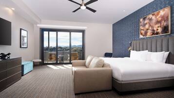 Una habitación de hotel moderna con una cama grande, un ventilador de techo, un sofá, un televisor y un balcón con vistas.