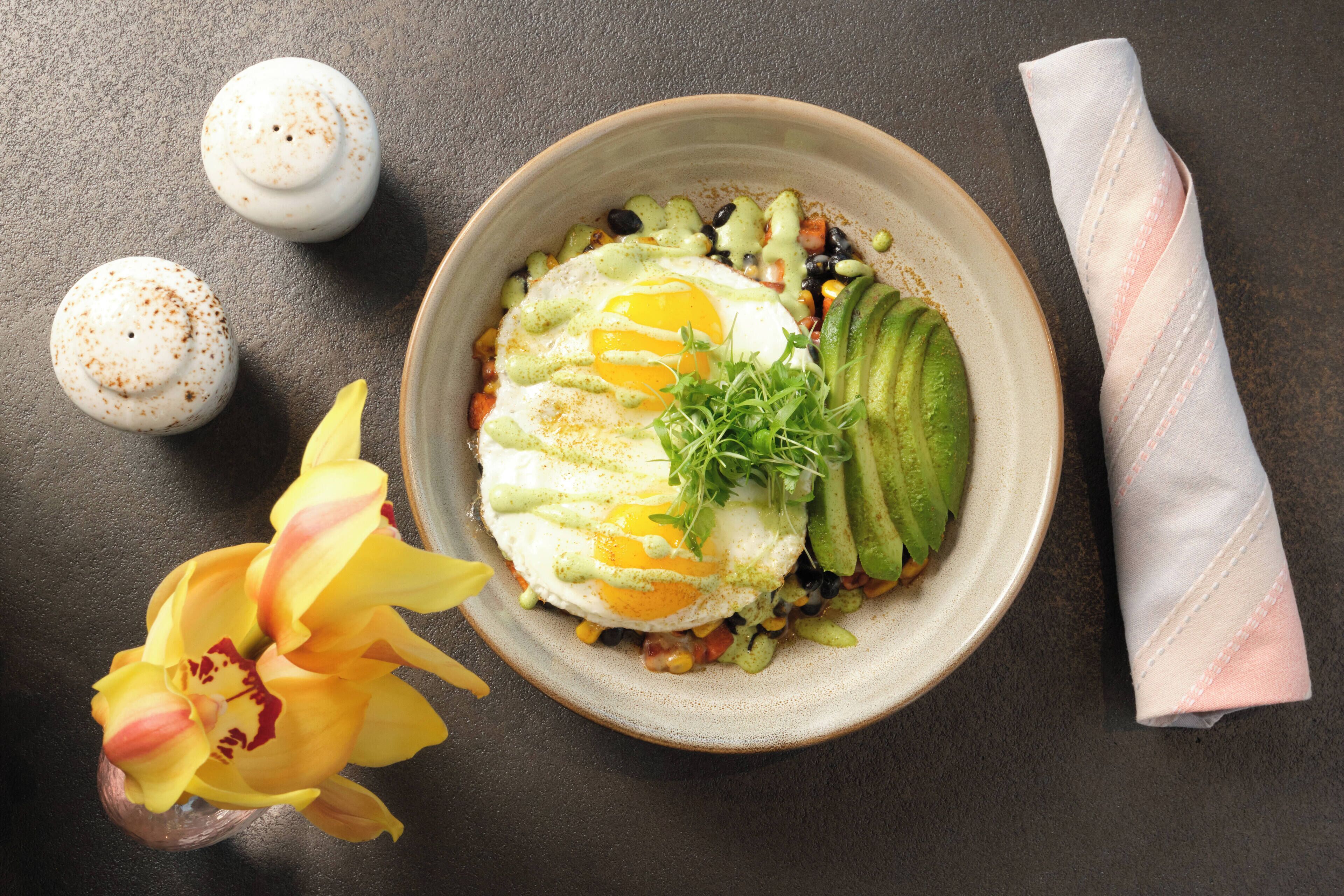 Un plato con comida que incluye una loncha de aguacate, un huevo y vegetales verdes.