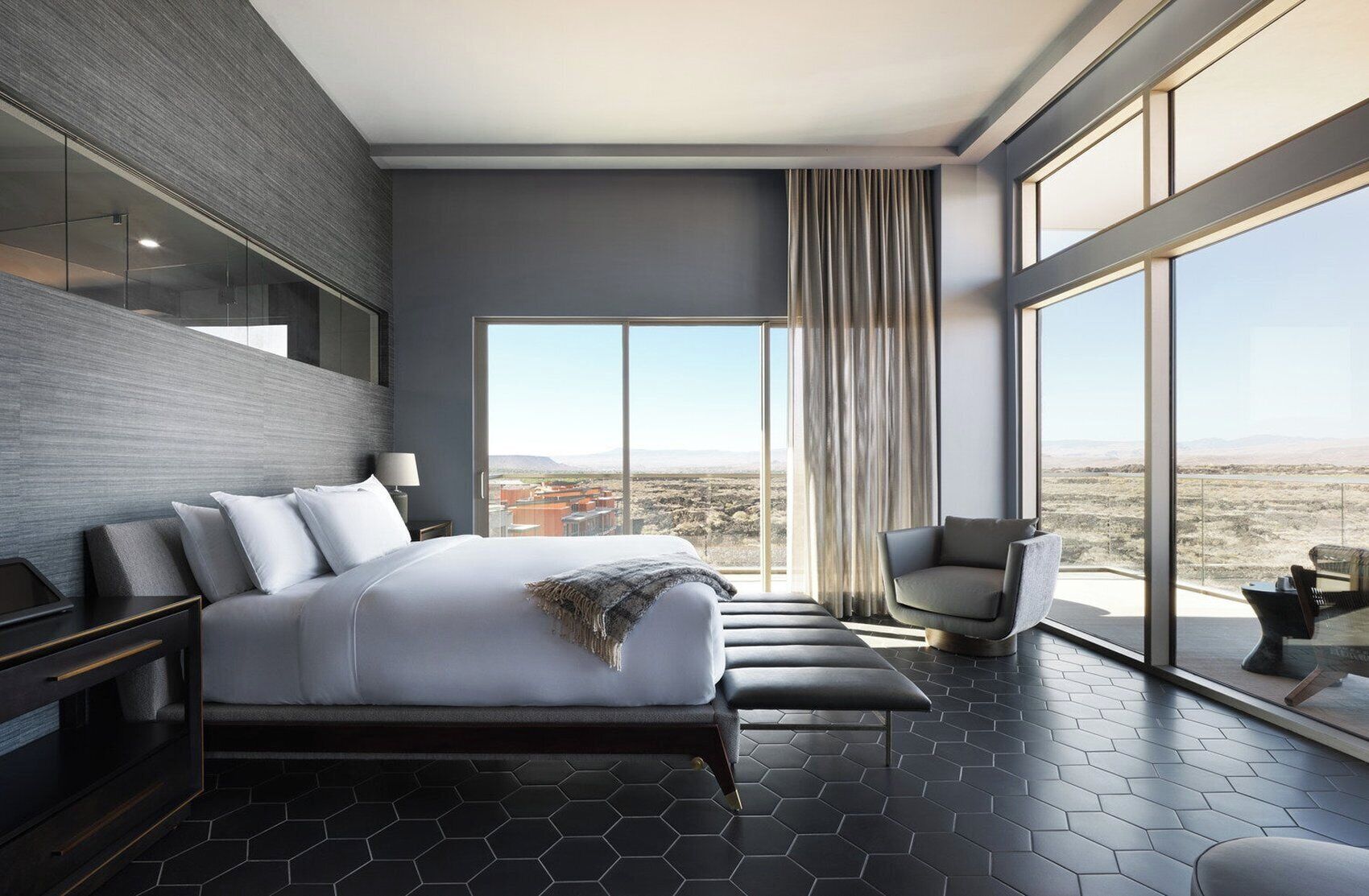 A modern hotel room with a large bed, a seating area, and a view of the desert landscape.