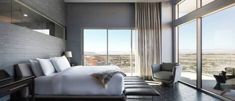 A modern hotel room with a large bed, a seating area, and a view of the desert landscape.