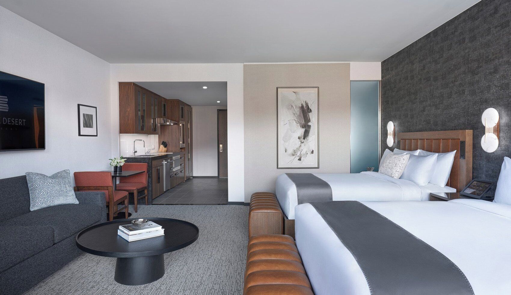 Una habitación de hotel moderna con sofá, mesa de centro, cama con cabecera, escritorio y zona de cocina.