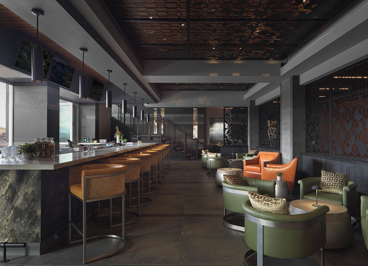 Un bar moderno con una barra alargada, varios taburetes y una escalera que sube a un nivel superior.