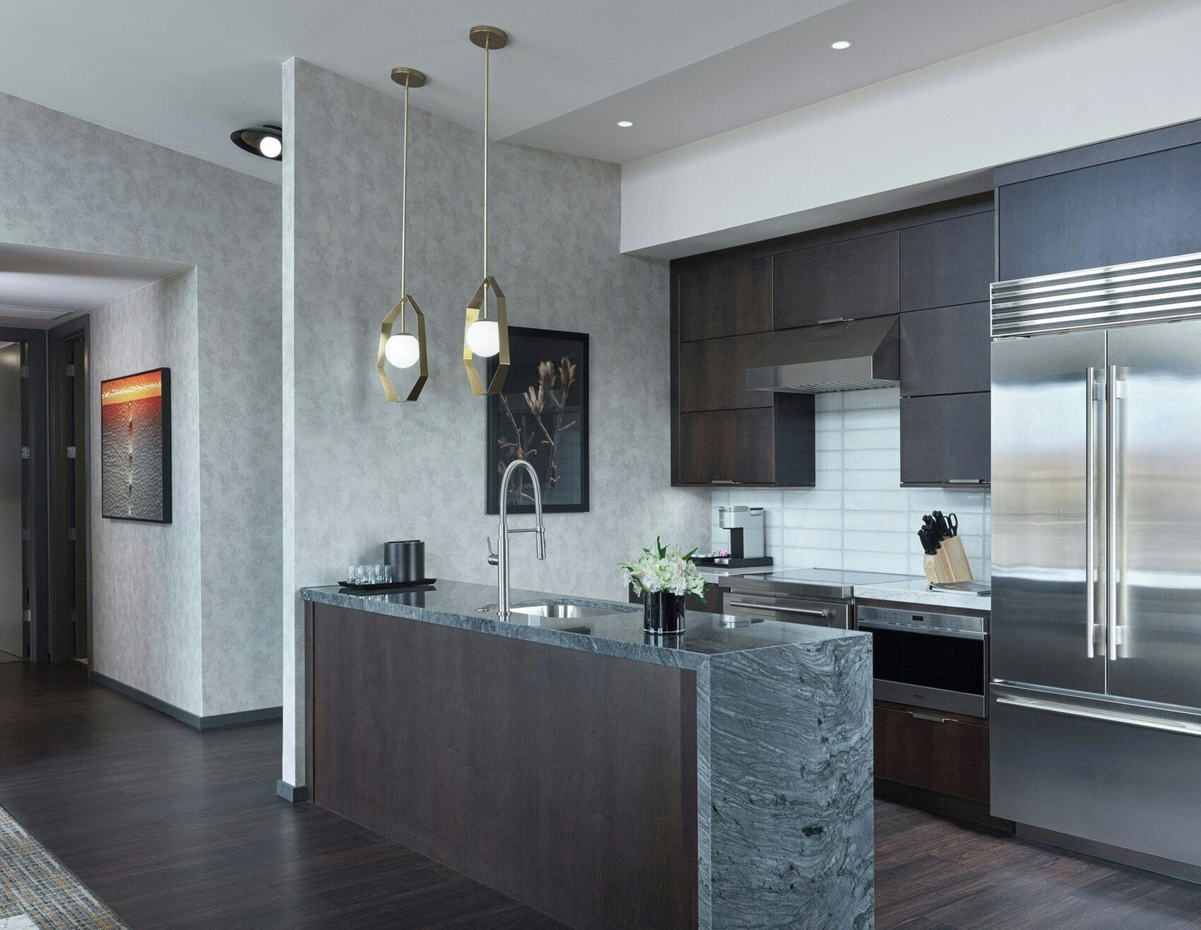 Una cocina moderna con una isla central, electrodomésticos de acero inoxidable e iluminación colgante.