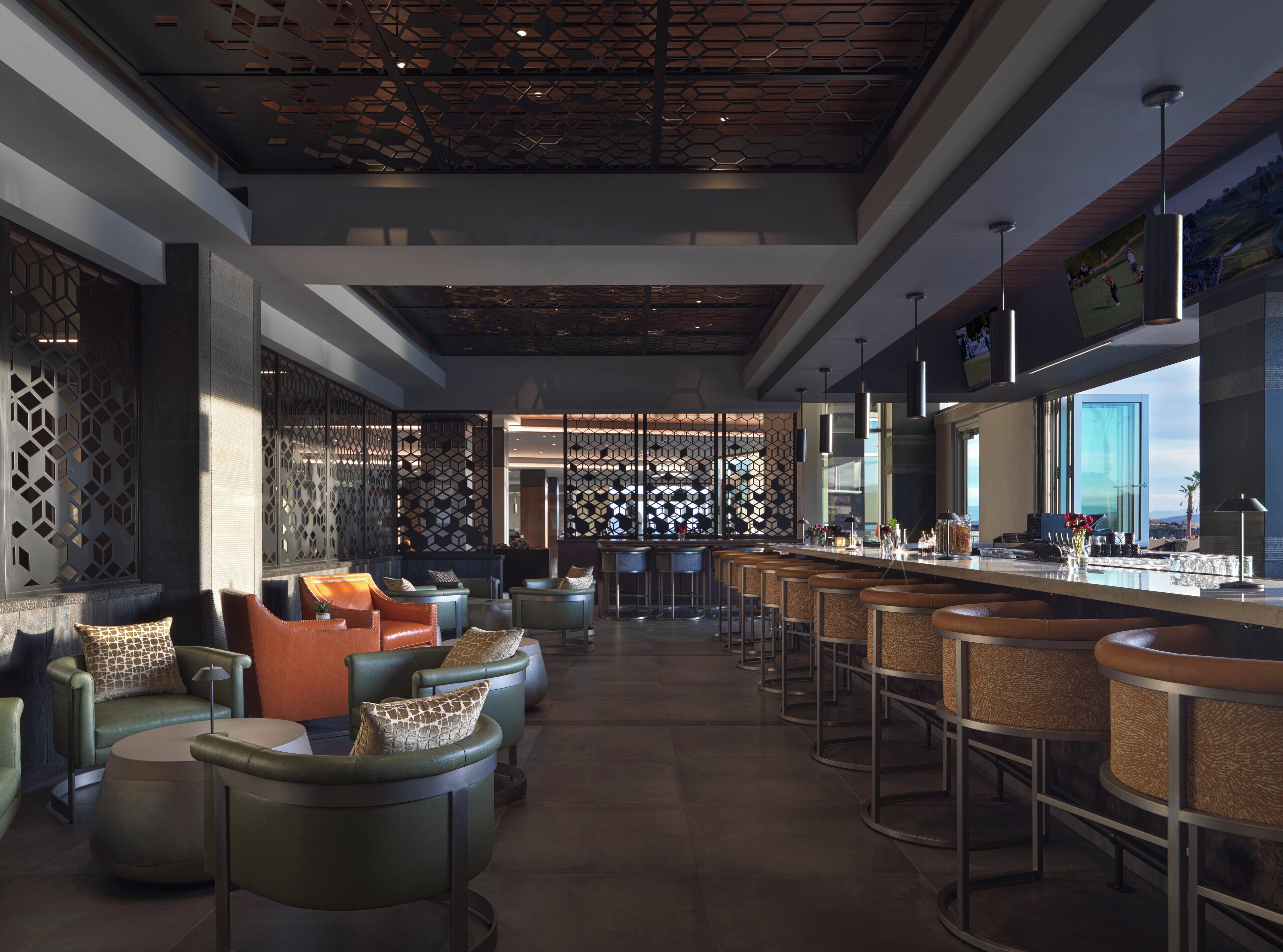 Eine moderne Bar mit Ledersitzgelegenheiten, einer hohen Decke mit geometrischen Mustern und Blick ins Freie.
