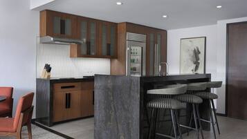 A modern kitchen with wooden cabinets, a central island with stools, a stainless steel range hood, and a refrigerator.