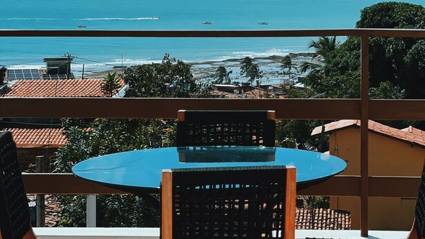 Ein Balkon mit Tisch und Stühlen mit Blick auf einen Strand, auf dem Boote liegen, und einen klaren Himmel.