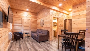 A log cabin interior with a sofa, chairs, a table, a TV mounted on the wall, and a wooden floor. - White Mountains Family Cabin, 4BR and Loft (Bethlehem)