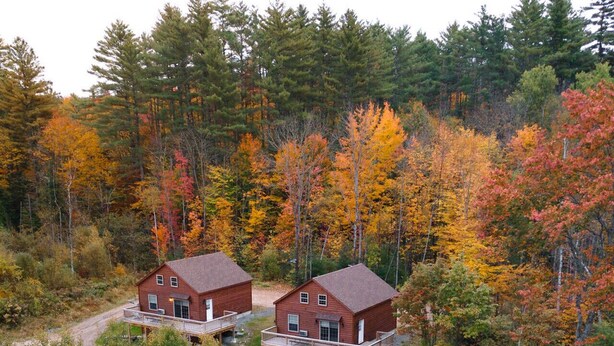 Two wooden cabins with attached porches, surrounded by a forest with autumn foliage. - White Mountains Family Cabin, 4BR and Loft (Bethlehem)