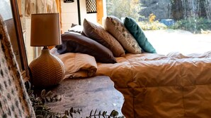 A wooden interior with a bed, a lamp, macrame wall decor, and a view of trees.