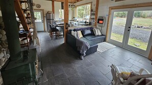 A cozy cabin interior with a dining area, kitchen, and a large window overlooking a yard.