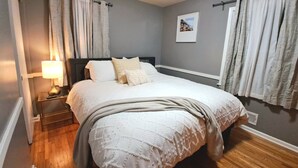 A neatly made bed with a white comforter and a beige throw blanket, a bedside lamp, and a framed picture on the wall.