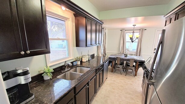 A kitchen with dark cabinets, a stainless steel refrigerator, and a dining area with a table and chairs.