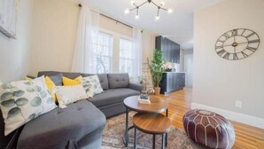 Una sala moderna con un sofá modular, una mesa de centro redonda y un otomano decorativo.