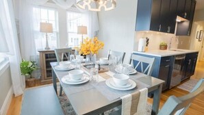Una cocina moderna con gabinetes oscuros, una mesa de comedor preparada para cuatro personas y una araña.
