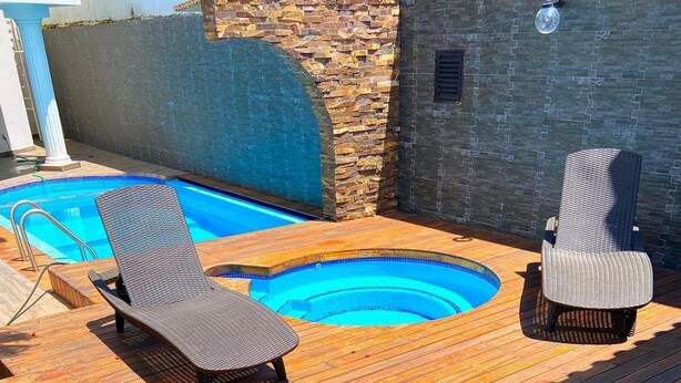 A wooden deck with a swimming pool, two lounge chairs, and a stone wall.