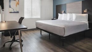 Une chambre d’hôtel moderne, dotée d’un grand lit, d’un bureau et d’une fenêtre avec stores.