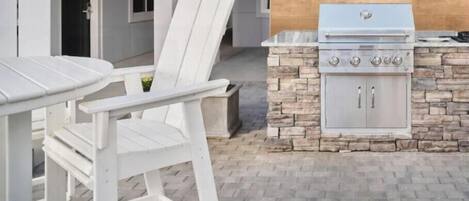 Un patio al aire libre con una parrilla de piedra, sillas blancas y una mesa.