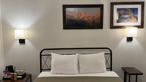A hotel room with a bed, two wall-mounted lamps, and two framed pictures on the wall. - Eastern Sierra Motor lodge (Independence)
