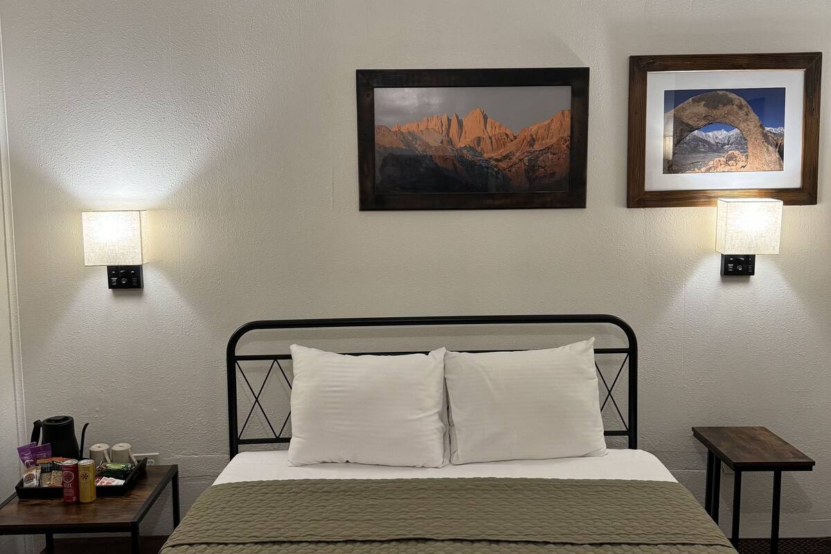 A hotel room with a bed, two wall-mounted lamps, and two framed pictures on the wall.