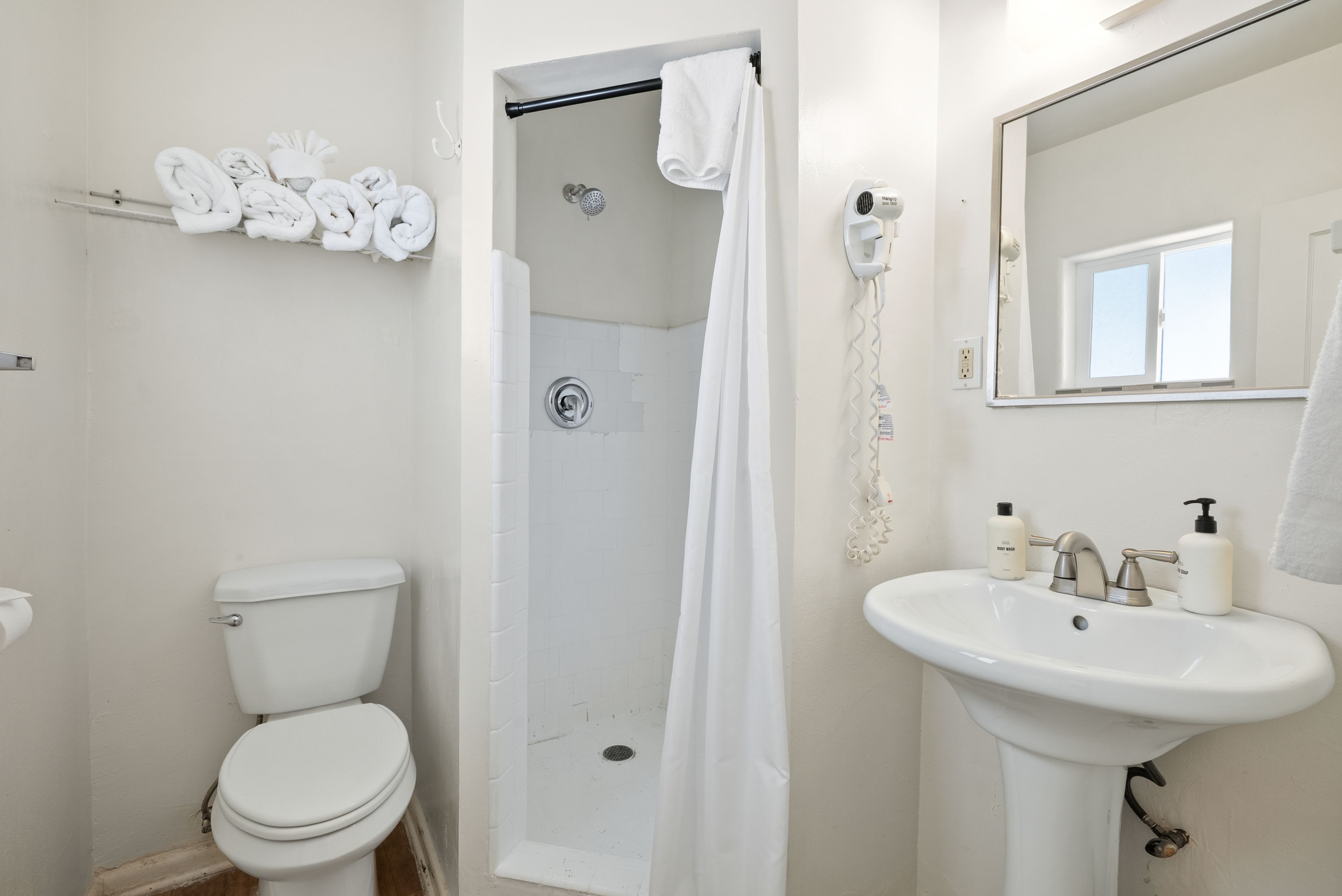 A bathroom with a toilet, a shower with a curtain, a sink with soap, and a mirror.