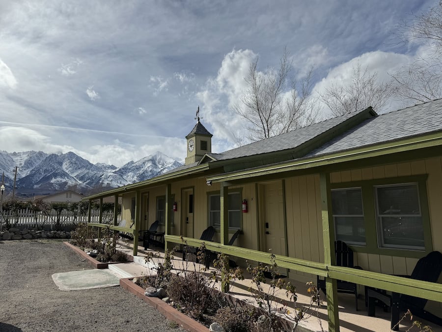 A building with a clock tower, a covered outdoor seating area, and a view of snow-capped mountains.