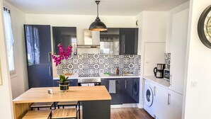 A modern kitchen with a central island, black cabinets, a washing machine, and a decorative tile backsplash.