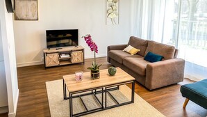 A living room with a TV, sofa, coffee table, and a large window with curtains.