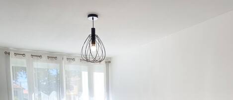 Une chambre moderne avec un grand lit, une table de chevet avec une lampe et une fenêtre ornée de rideaux légers.