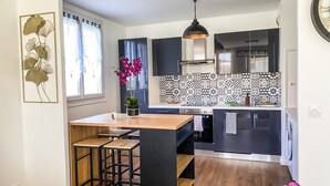 A modern kitchen with a central island, bar stools, a pendant light, and a patterned backsplash.