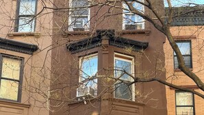 A brownstone building with a central entrance, large windows, and a car parked in front.
